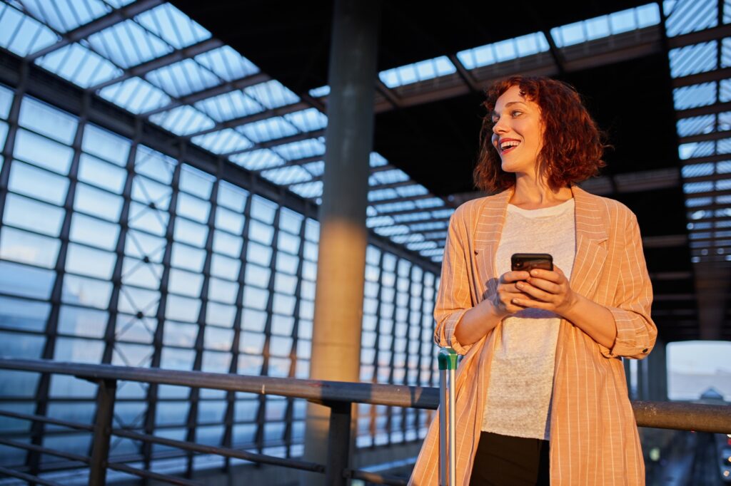 Smiling young woman browsing phone at station